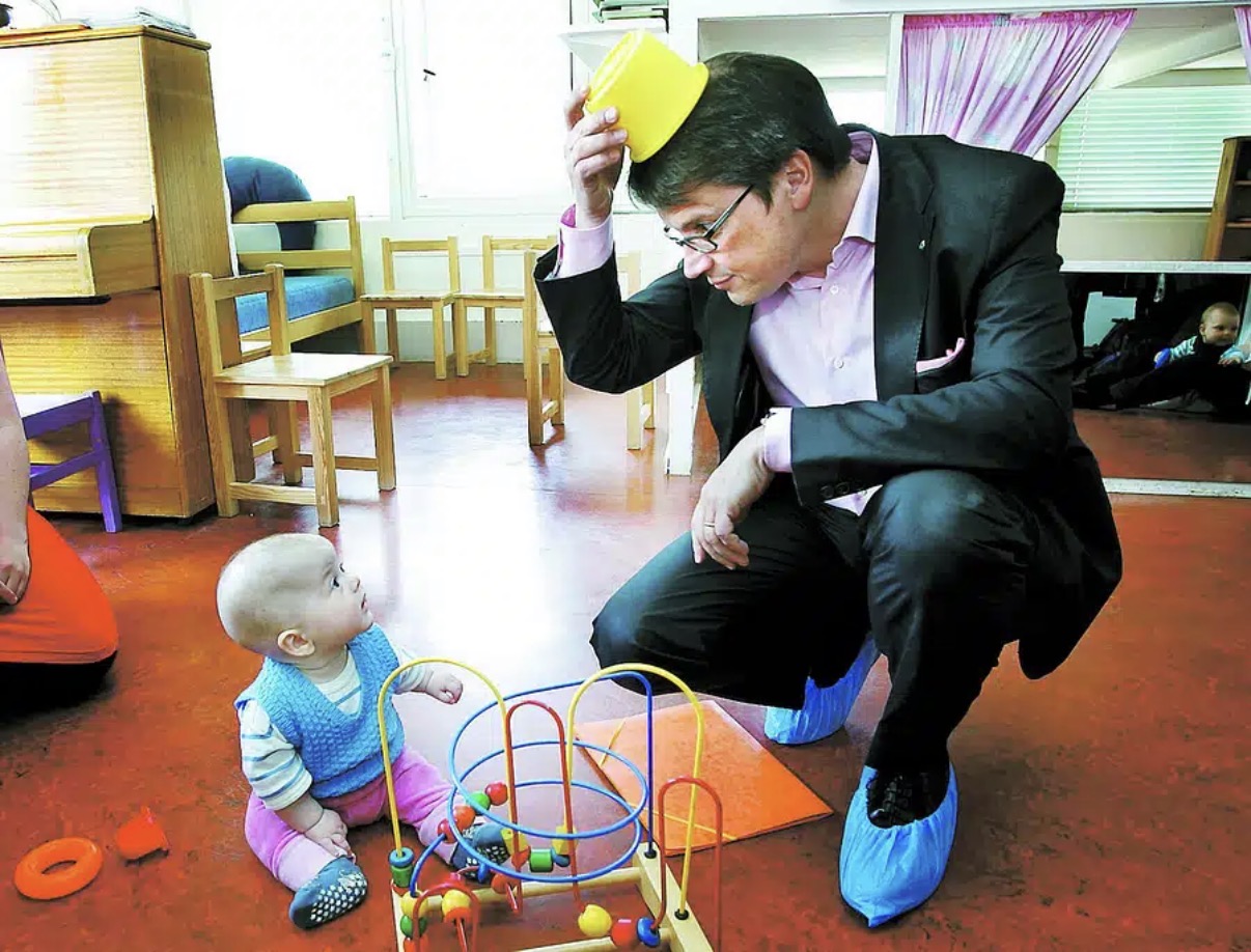 A man putting a yellow bucket on his head in front of a baby